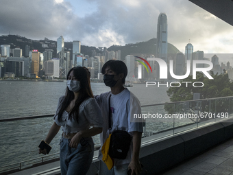 A Couple wearing face masks walks pass the Hong Kong City Skyline in Hong Kong, Monday, May 10, 2021. (