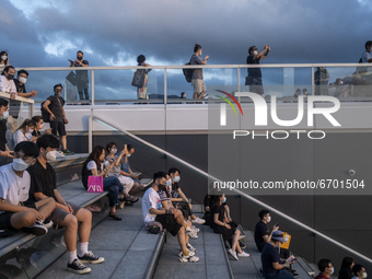 People wearing face masks sits on stairs while looking at the sunset in Hong Kong, Monday, May 10, 2021. (