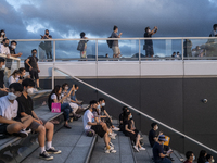 People wearing face masks sits on stairs while looking at the sunset in Hong Kong, Monday, May 10, 2021. (