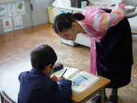 An elementary student practices Korean letters as a teacher wearing a traditional dress conducts a Korean lesson at Hiroshima Korean School...