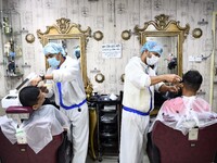 Barbers wearing personal protective equipment serve their clients in a salon at Rampura in Dhaka, Bangladesh on May 12, 2021 amid the corona...
