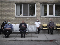 Iranian elderly people wearing protective face masks sit in an outdoor area while waiting to receive a dose of the new coronavirus disease (...