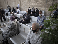 Iranian elderly people wearing protective face masks sit in an outdoor area while waiting to receive a dose of the new coronavirus disease (...