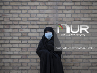 An Iranian elderly woman wearing a protective face mask stands in an outdoor area while waiting to receive a dose of the new coronavirus dis...