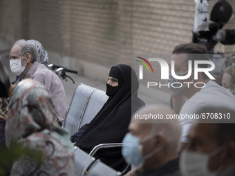 An Iranian elderly woman wearing a protective face mask sits in an outdoor area while waiting to receive a dose of the new coronavirus disea...