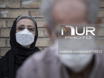 An Iranian elderly woman wearing a protective face mask looks on as she sits in an outdoor area while waiting to receive a dose of the new c...