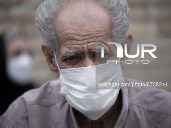 An Iranian elderly man wearing a protective face mask looks on as he sits in an outdoor area while waiting to receive a dose of the new coro...