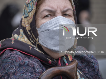 An Iranian elderly woman wearing a protective face mask looks on as she sits in an outdoor area while waiting to receive a dose of the new c...