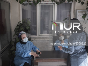 An Iranian medical personnel wearing a protective suit talks to a woman who has bring her mother (Not pictured) to receive a dose of the new...