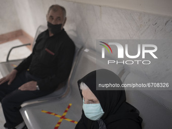 An Iranian elderly woman wearing a protective face mask sits at a corridor while waiting to receive a dose of the China's Sinopharm new coro...