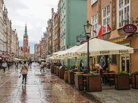 People walking by the rainy old city of Gdansk Dluga street along the newly open after the covid-19 lockdown open air restaurants are seen i...