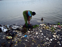 An Indian woman finds the coins and other valuable things  which devotees offer during prayers on the polluted  river banks of River Ganges,...