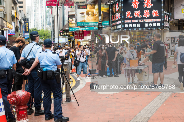 Police monitor an activist member of trade unions talking to livestreamers in Causeway Bay. The activist holds a representation of Victoria...