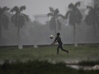 A boy plays football during rain at a park area in Dhaka, Bangladesh on June 11, 2021. (
