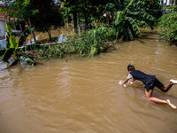 South Tangerang, Banten, Indonesia, 12 June 2021 :A teenager seemed to be enjoying the overflowing river due to its blocked flow.. Floods th...