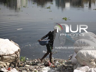 A worker cleans and collects parts from plastic bottles to be recycled later in the river Buriganga in Dhaka, Bangladesh on June 14, 2021. B...