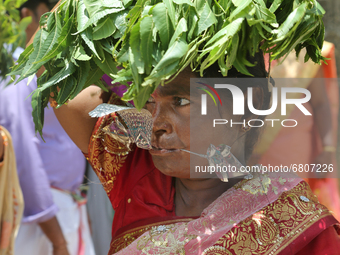 Tamil Hindu woman with a facial skewer and pins in her arm as she carries a pot on her head filled with milk and honey and covered with marg...