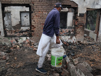 A Kashmiri resident carry the water bucket to douse fire inside a damaged residential house where three militants were killed in a military...