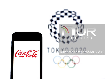 In this photo illustration a Coca-Cola logo seen displayed on a smartphone with a Tokyo 2020 Olympic Games logo in the background. (
