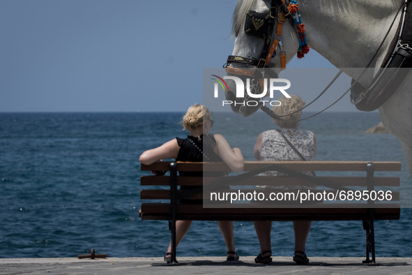 Two women are sitted on a bench in the center of Chania, Greece at the Old Venetian Harbour during rising temperatures on July 22, 2021.  