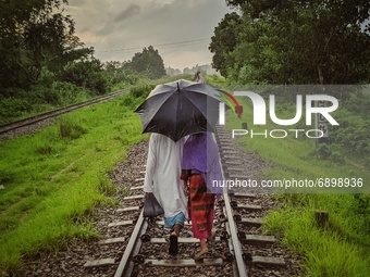 People walks through railroad during raining in a rural area of Bangladesh on July 24, 2021. (