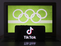 TikTok logo is displayed on a mobile phone screen photographed with Olympic rings symbol on the background for illustration photo. Leszczewe...