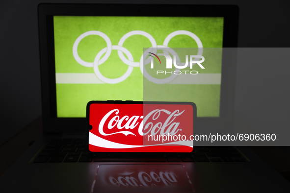  Coca-Cola logo is displayed on a mobile phone screen photographed with Olympic rings symbol on the background for illustration photo. Leszc...