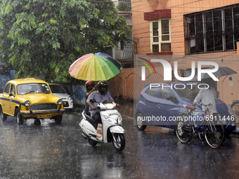 A woman holds an umbrella as she rides a scooty during heavy rainfall in Kolkata, India, 28 July, 2021.  (