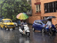 A woman holds an umbrella as she rides a scooty during heavy rainfall in Kolkata, India, 28 July, 2021.  (