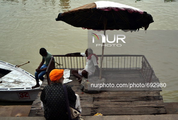 Indian boatmen sit under a wooden umbrella on the Banks of River Ganges at Assi Ghat in Varanasi on July 16,2015. 