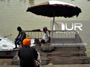 Indian boatmen sit under a wooden umbrella on the Banks of River Ganges at Assi Ghat in Varanasi on July 16,2015. (