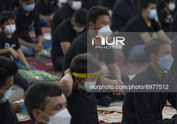 An Afghan refugee young boy wearing a protective face mask wears a religious headband while attending with his father at a Muharram mourning...