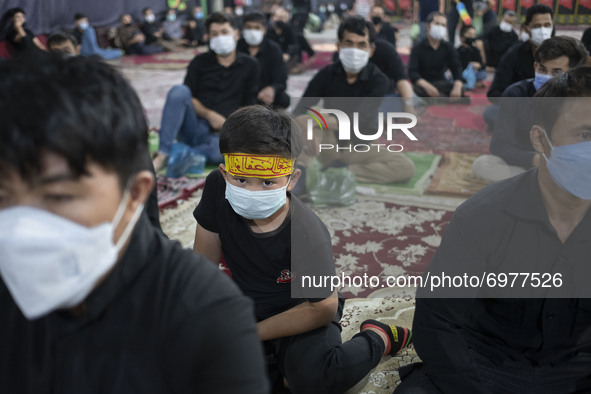An Afghan refugee young boy wearing a protective face mask and a religious headband looks on while attending a Muharram mourning ceremony fo...