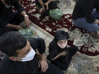 An Afghan refugee young girl wearing a protective face mask looks on as she sits next to her father while attending a Muharram mourning cere...