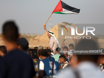 An elderly Palestinian man raises a national flag as youths shout slogans during a protest along the border fence, east of Khan Yunis in the...