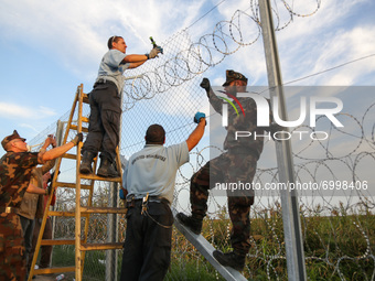 Hungarian soldiers and workers erect a barbwire fence as Hungarian police officers close the border line between Serbia and Hungary in Roszk...