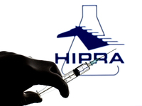 In this photo illustration, a close up of a hand holding a medical syringe in front of the Hipra, S.A. logo (