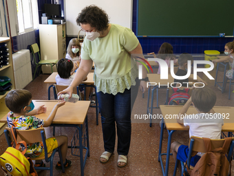 A teacher with a face mask puts some hydro alcoholic gel in the hands of a student during the new opening of the Primary School Year at CEIP...