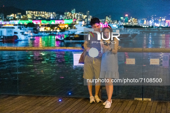 Hong Kong, China, 21 Sep 2021,  A young couple take selfies in front of the illuminations of Victoria Harbour on Kwun Tong Promenade. 