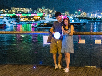 Hong Kong, China, 21 Sep 2021,  A young couple take selfies in front of the illuminations of Victoria Harbour on Kwun Tong Promenade. (