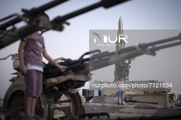 Iranian young girls pose with a military tank and an anti-aircraft gun while visiting a war exhibition which is held and organized by the Is...