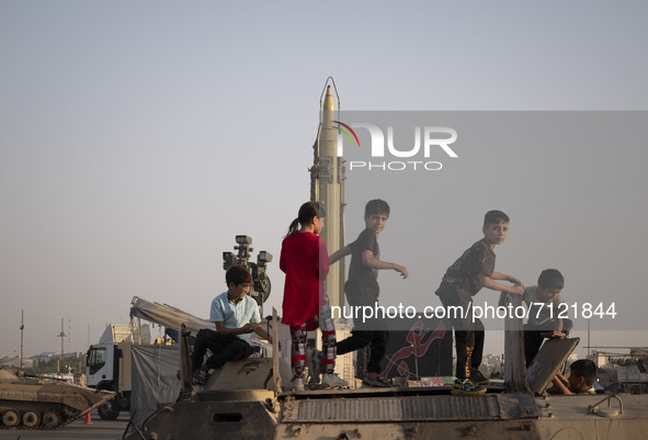 Iranian children play with a military personnel carrier as an Iranian long range surface to surface Qadr missile is displayed in a war exhib...