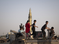 Iranian children play with a military personnel carrier as an Iranian long range surface to surface Qadr missile is displayed in a war exhib...