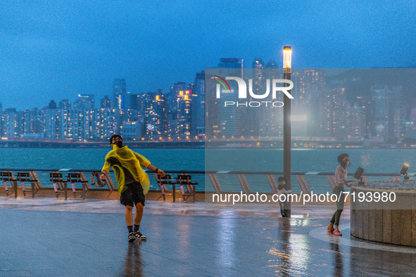 A young man poses for a picture on the Avenue of  Stars in Tsim Sha Tsui, while children are buffeted by the wind, in Hong Kong, China, on O...