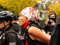 A Native American cries for the crimes against her people, and then in physical pain, as she is handled roughly by United States Secret Serv...