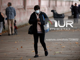 A woman wearing a face mask walks beside the National Covid Memorial Wall on the south bank footpath of the River Thames opposite the Houses...