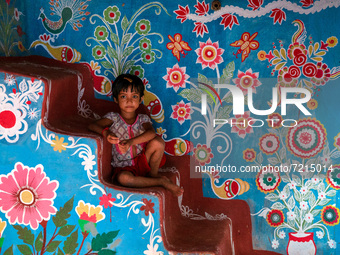 A child poses in front of a colorfully painted house in alpona village in chapainawabganj, Bangladesh. (