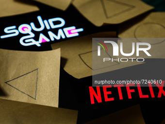 Netflix and Squid Game series logos displayed on a phone screens are seen with symbols known from the series, drawn on pieces of paper, in t...