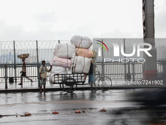 Indian Laborers push a cycle van loaded vegetable cover the plastic protects rain across the Howrah Bridge during heavy rainfall in Kolkata,...