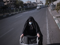 An Iranian elderly veiled woman wearing a protective face mask walks along an avenue with walker to the University of Tehran for taking part...